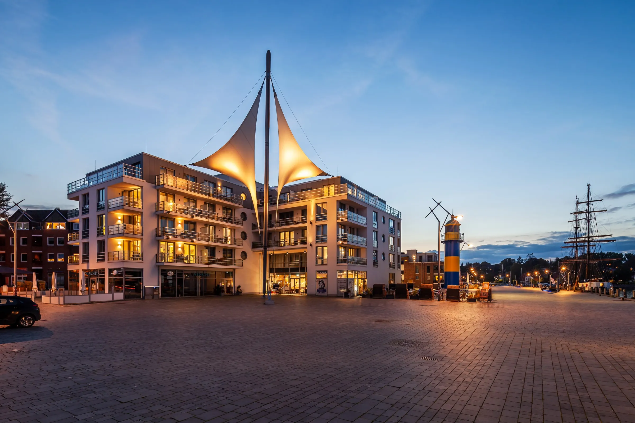 Das Haus mit den Segeln an der Hafenspitze in der blauen Stunde, die Fenster leuchten