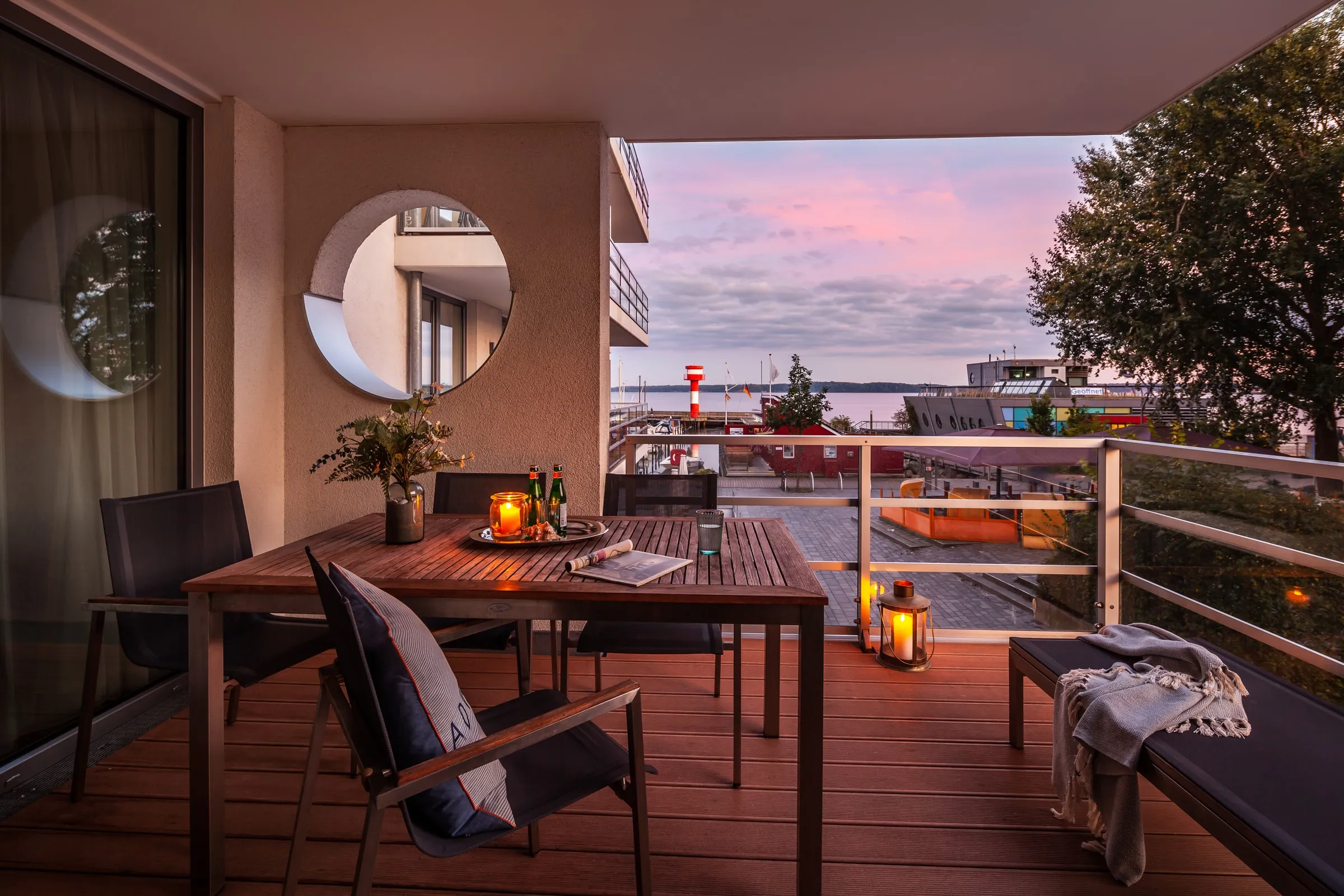 Die Loggia im Abendlicht, Windlichter auf dem Tisch, der Himmel über dem Hafen rosa
