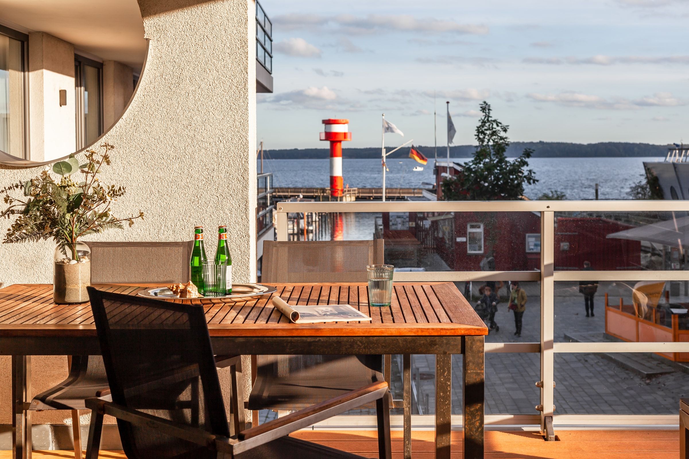 Der gedeckte Teaktisch auf der Loggia, dahinter der Leuchtturm an der Hafeneinfahrt