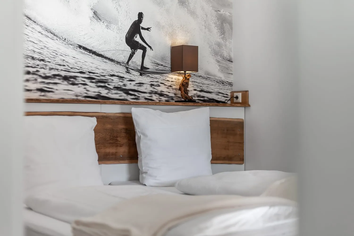 Kopfteil aus Holz, weiße Kissen und das Schwarzweißbild eines Surfers