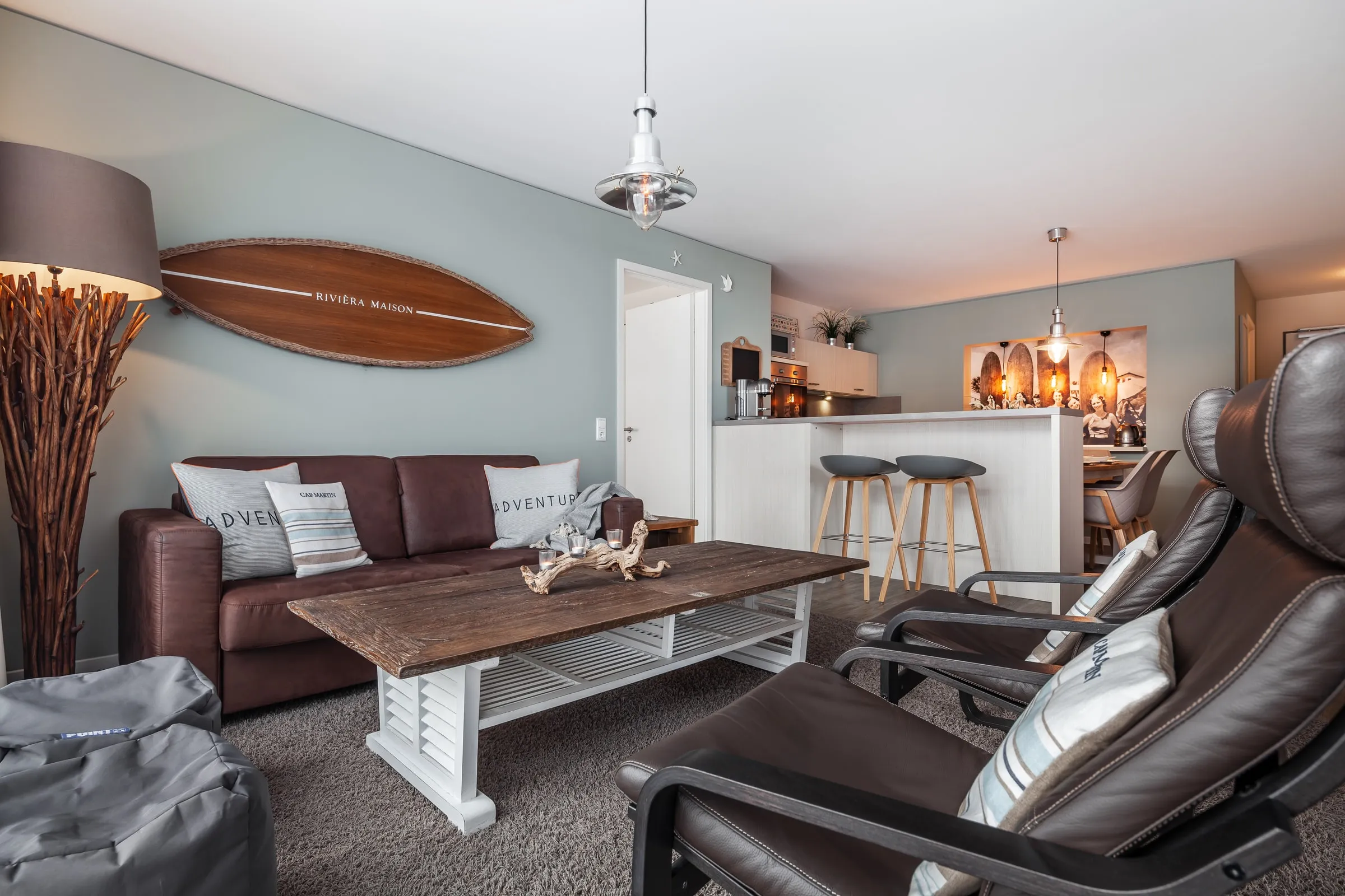 Die Sitzecke mit braunem Sofa, Couchtisch und Surfbrett an der Wand, hinten der Esstisch